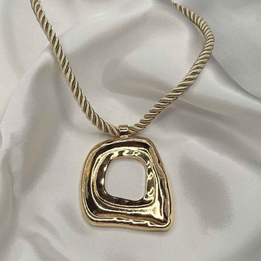 Gold necklace with a square pendant on a white fabric background